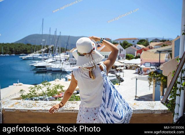 a tourist woman with hat enjoy view of idyllic village of fiskardo, kefalonia, greece, during summer vacation time