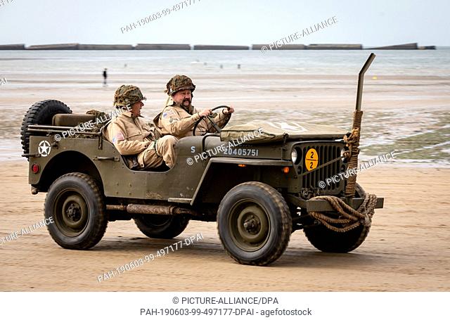 03 June 2019, France (France), Arromanches-Les-Bains: In a historic jeep, men in US-American uniforms from the time of the Second World War drive across the...