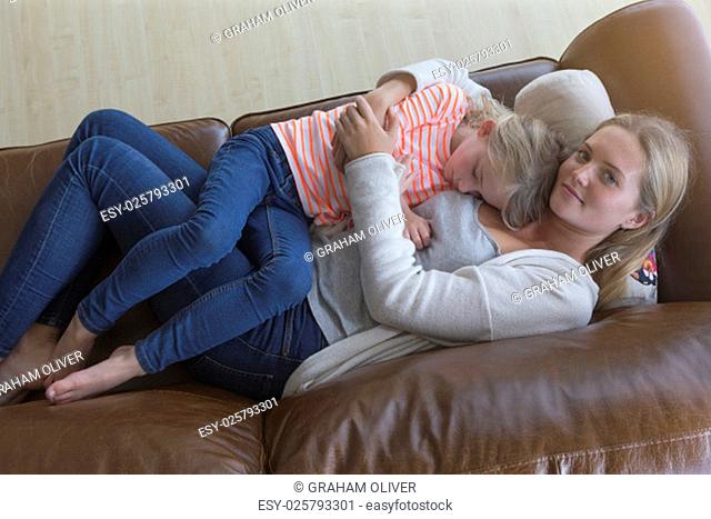 Ariel view of a mother cuddling her tired daughter on a sofa at home