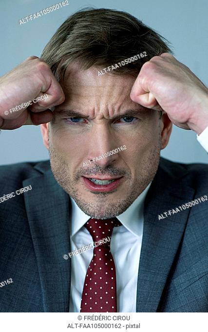 Businessman holding clenched fists against head in anger, portrait