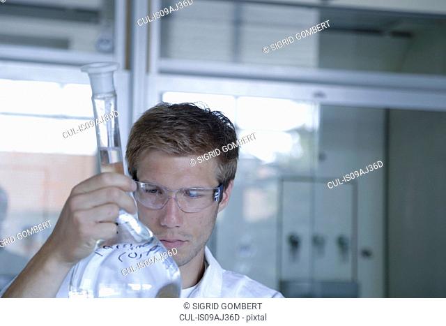Young male scientist analyzing volumetric flask in lab