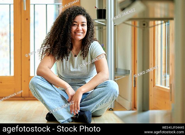 Smiling young woman sitting cross-legged on floor at home