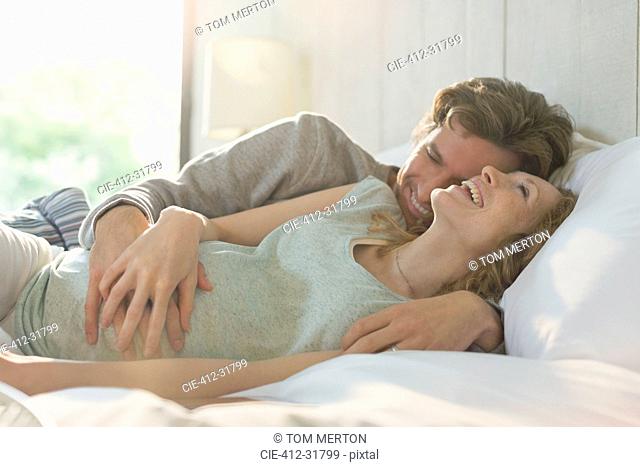 Affectionate pregnant couple laying in bed laughing