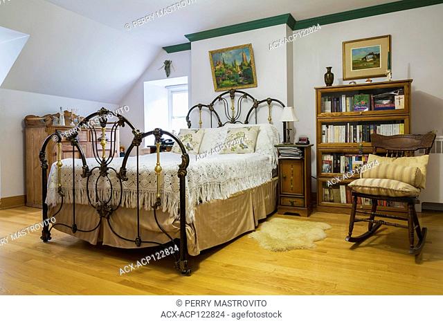 Double bed with antique forged aluminium and brass headboard and footboard in upstairs master bedroom inside an old 1839 Canadiana fieldstone style house
