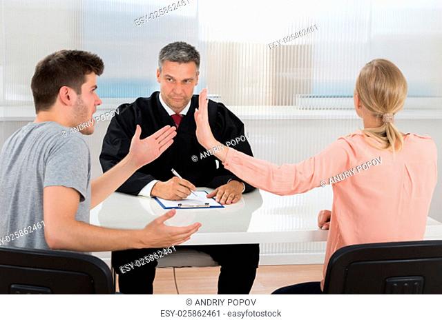 Young Couple Having An Argument In Front Of Male Judge At Desk