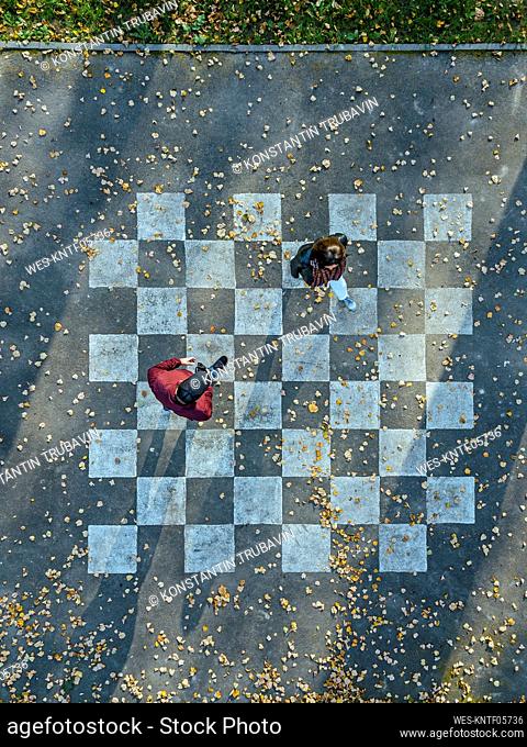 Man and woman walking on asphalt painted with chessboard pattern