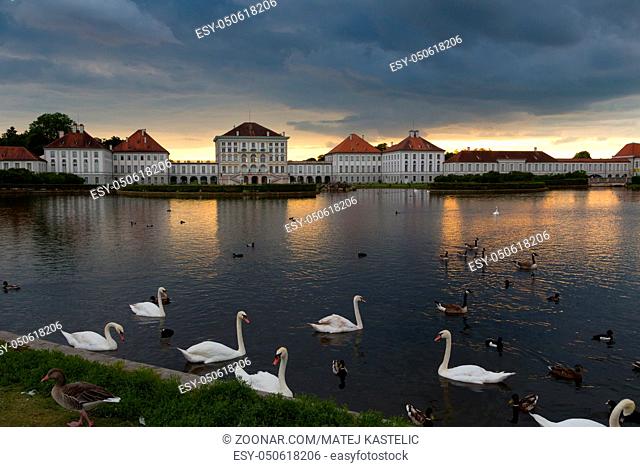 Dramatic scenery of Nymphenburg palace in Munich Germany. Sunset after the sorm. White swans and duks swimming in pond in front of the palace