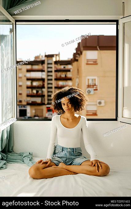 Afro woman sitting on bed cross-legged at home