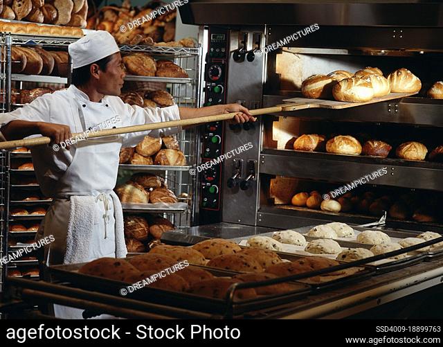 Baker feeding loafs of dough into industrial bakery oven