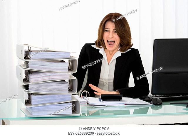 Irritated Young Businesswoman Looking At Stack Of Folders In Office