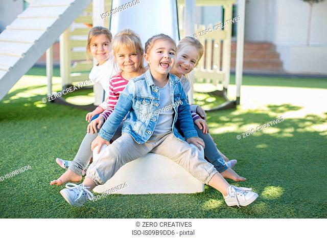 Girls and boys at preschool, portrait sitting on playground slide in garden