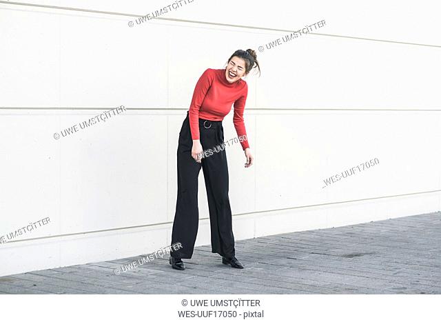 Laughing young woman standing in front of a wall