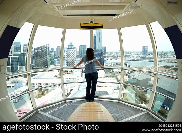 Rear view of woman standing in Melbourne Star Ferris wheel, looking at city skyline, Australia