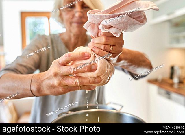 Making paneer, woman squeezing a cheesecloth filled with cream cheese and separating cheese from whey