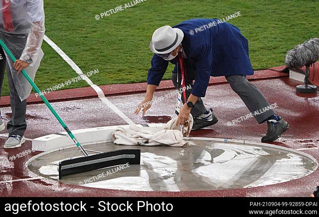 04 September 2021, Japan, Tokio: Paralympics: Athletics, men, finals, shot put, F63, at Olympic Stadium. Helpers clear the ring of rainwater