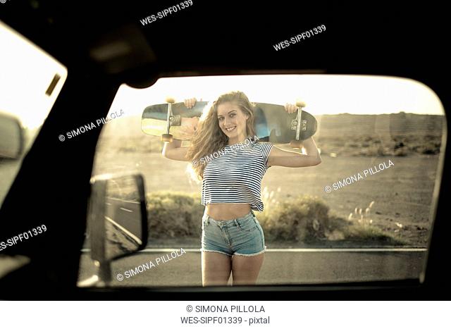 Spain, Tenerife, young woman with skateboard seen through car window