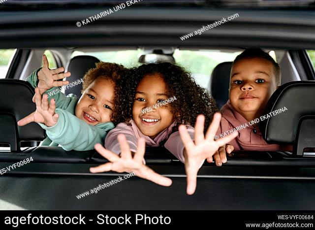 Smiling brothers and sister playing at car back seat