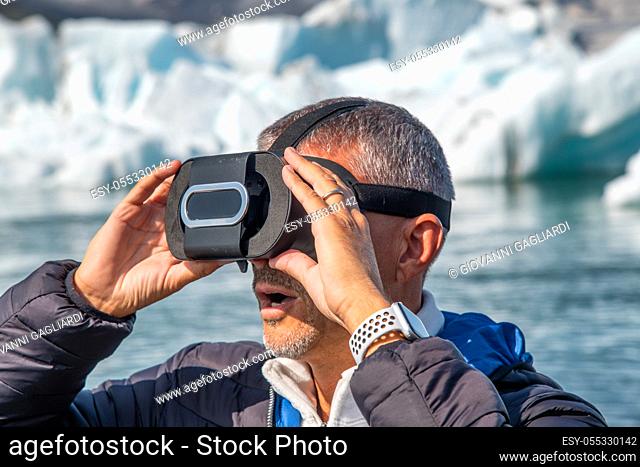 Astonished man wearing VR glasses with icebergs floating in the Jokulsarlon Lagoon, Iceland