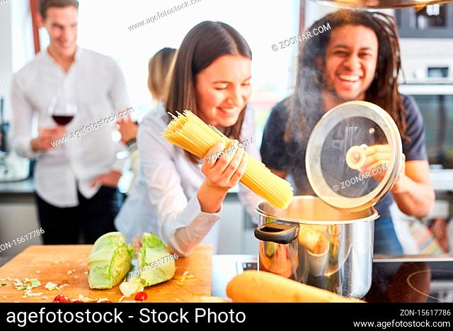 Lachende Freunde oder Paar am Herd in WG Küche beim Spaghetti Nudeln kochen