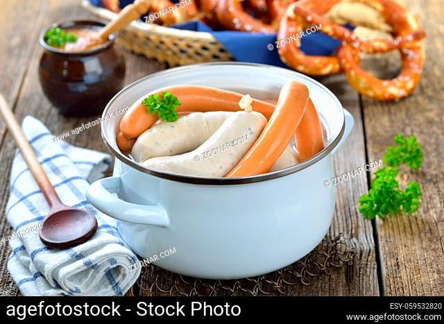 Frische Weißwürste und Wiener im Topf mit Brezen und süßem Senf serviert - Hot Bavarian white sausages in an enamel cooking pot served on a wooden table with...