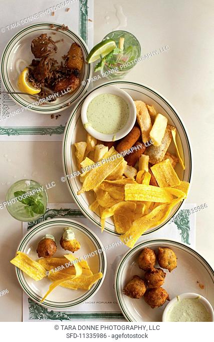 A platter of fried, sweet plantains, dill mayonnaise, empanadas and fried yuca sticks with pork with rice and beans, fish croquettes and mojitos