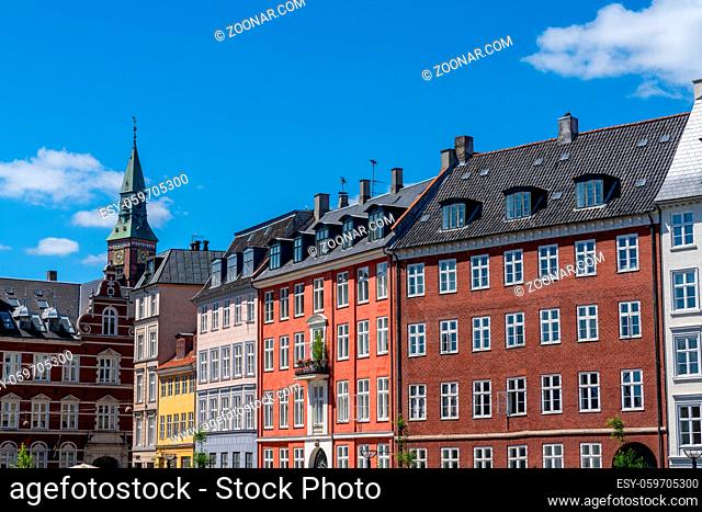Copenhagen, Denmark - 13 June, 2021: colorful historic cityscape and buildings with a church spire in the background under a blue sky with white cumulus clouds