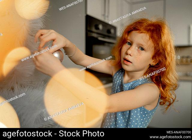 Redhead girl decorating Christmas tree with ornament at home