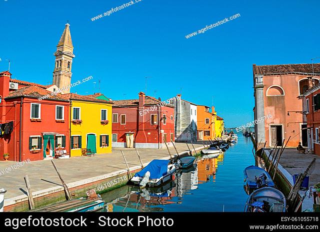 Overview of colorful buildings, bell tower and boats in blue sunny day, facing a canal at Burano, a gracious little town full of canals, near Venice
