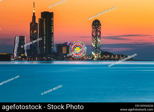 Batumi, Adjara, Georgia. Skyline Of Resort Town At Sunset Sunrise. Bright Orange Evening Sky. View From Sea To Illuminated Cityscape With Modern Urban...