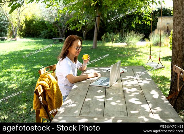Smiling freelancer sitting with coffee cup and working on laptop