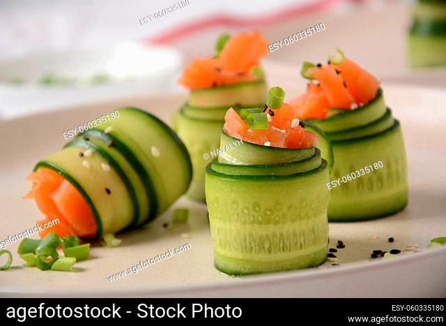 Cucumber rolls with pieces of salted salmon, black and white sesame seeds, chopped green onion. Holiday vegetable appetizers