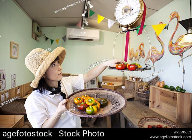 Japanese woman wearing hat working in a farm shop, weighing fresh vegetables