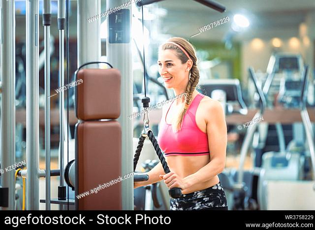 Happy and beautiful fit woman wearing pink fitness bra while exercising cable rope triceps extension at the gym