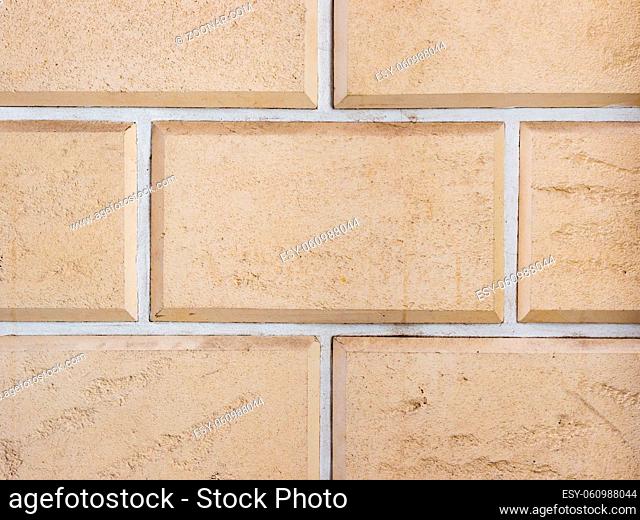 a wall from an artificial beige stone facade with rough fractured surfaces, laid as a brick