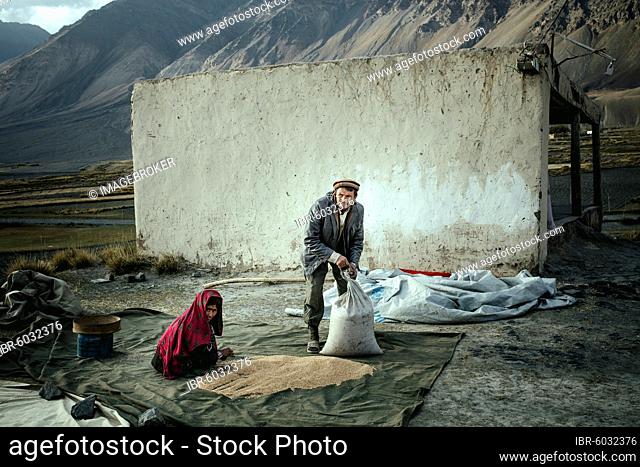 Man and woman filling threshed wheat into bags, members of the ethnic group of the sedentary Wakhi, Saradh-e-Broghil, Wakhan Corridor, Afghanistan, Asia