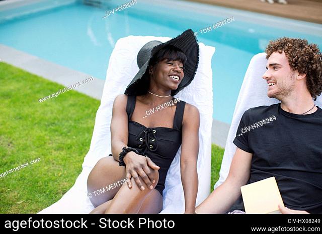 Happy young couple relaxing in lounge chairs at poolside