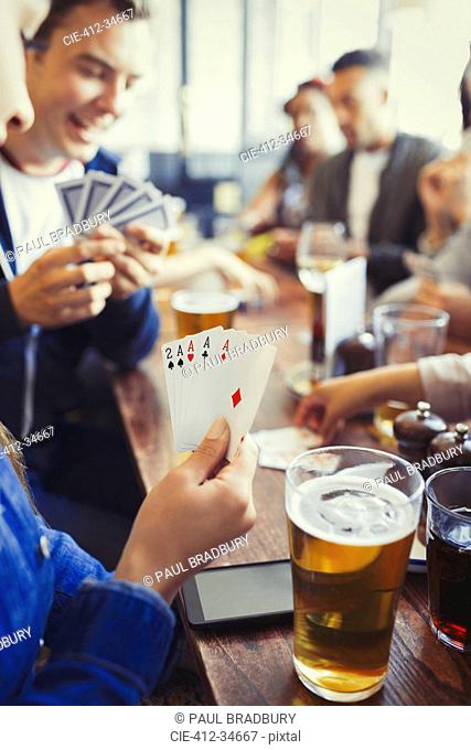 Woman holding aces four of a kind playing poker and drinking beer with friends at bar