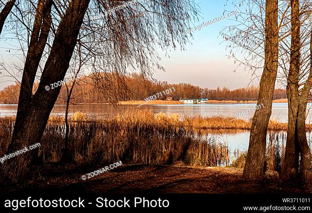 View of a little house close to the Dnieper river in Kiev, Ukraine, in winter under a clean blue sky. Trees and reeds in the forground