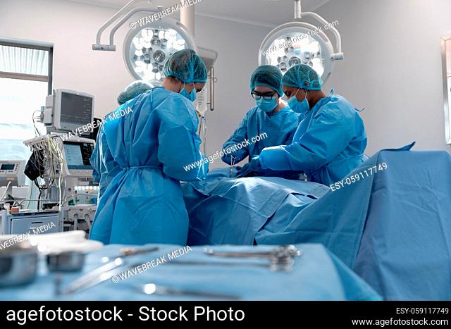 Diverse group of male and female surgeons in operating theatre wearing face masks performing surgery