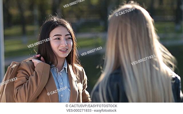 Cheerful asian girl gossiping with female friend