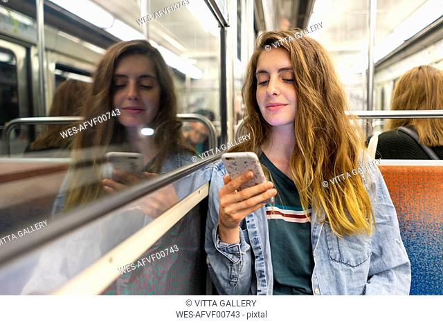 Smiling young woman in underground train looking at smartphone