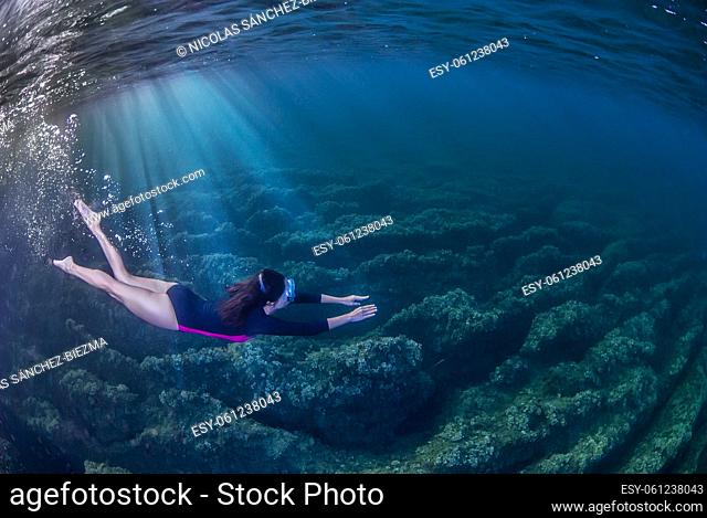 Woman swimming underwater in the Mediterranean. Rays of light entering the water from the left