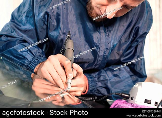 Close up Car glaze worker fixing and repairing a windshield or windshield of a car at a garage service station. Drill glass for repair
