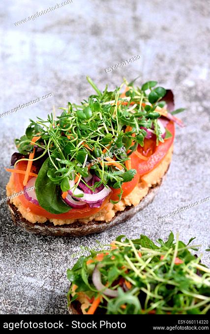 Sandwich toasted rustic bread with chickpea hummus, tomato slices, mix of lettuce and microgreens. Vegetarian breakfast