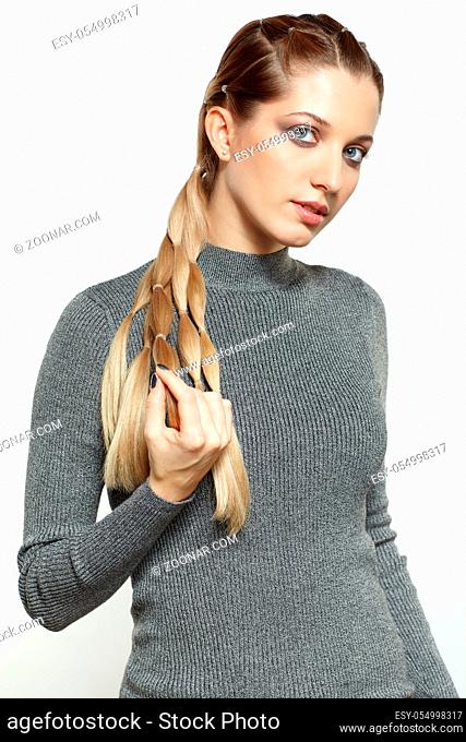 Portrait of beautiful young dark blonde woman. Female with creative braid hairdo on gray background. Girl holds braid in hand
