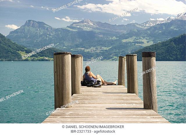 Woman sitting on a pier, hiking boots standing next to her, lakeside promenade, Weggis, Lake Lucerne, canton of Lucerne, Switzerland, Europe