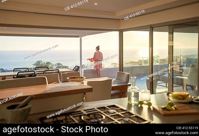 Woman in bathrobe relaxing on sunny luxury balcony with ocean view