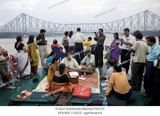 Musician performing on boat in river hooghly ; Howrah bridge now Rabindra Setu steel structure amazing feat of engineering ; Calcutta now Kolkata ; West Bengal...