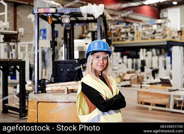 Confident engineer standing with arms crossed in factory