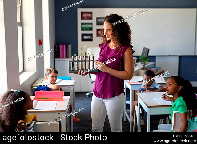 Caucasian young female teacher showing seedling test tubes to multiracial elementary children